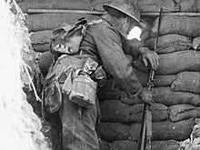 Visible parts of 1908 webbing in Battle Order are the haversack, which is being worn on the back in place of the valise, the entrenching tool carrier, the water bottle, and the ammunition pouches towards the front of his waist.